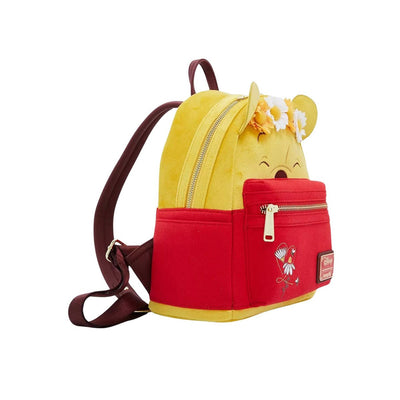 A side view of the yellow and red mini backpack featuring Winnie the Pooh's face with a floral crown. The backpack has brown straps and a small handle at the top.