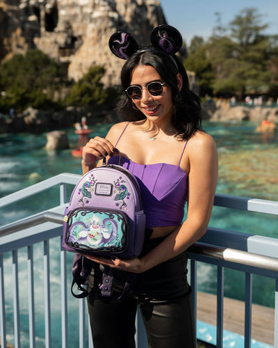671803390935 - 707 Street Exclusive - Loungefly Disney Villains Scenes Ursula Mini Backpack - Model Holding Loungefly Bag at Disneyland in Front of Matterhorn Mountain
